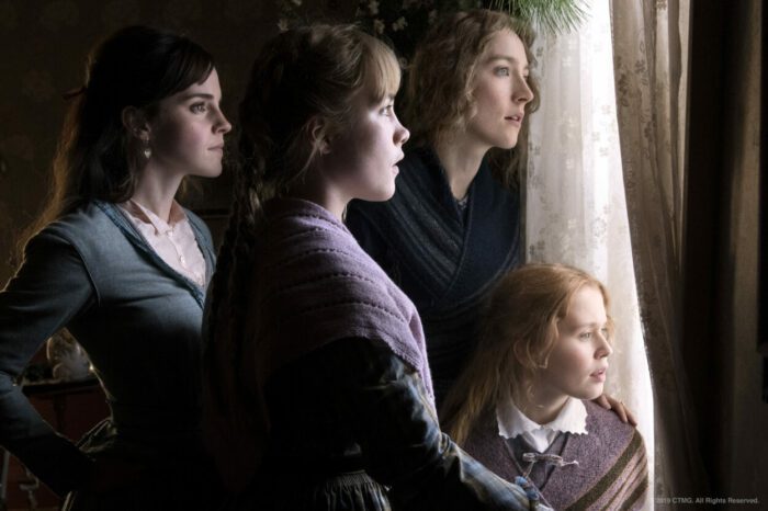 The March sisters of Little Women looking out a bright window, faces illuminated. 