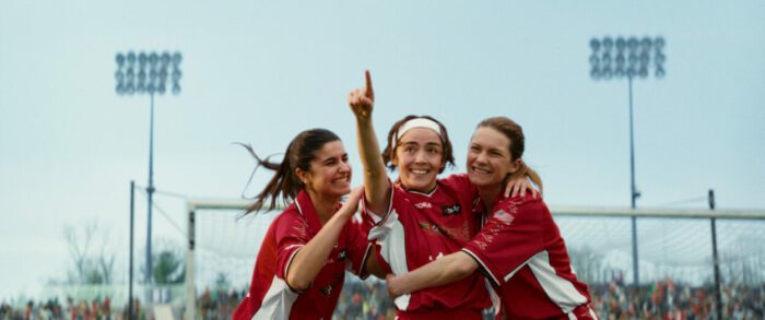 Three female soccer players in red kits celebrate.