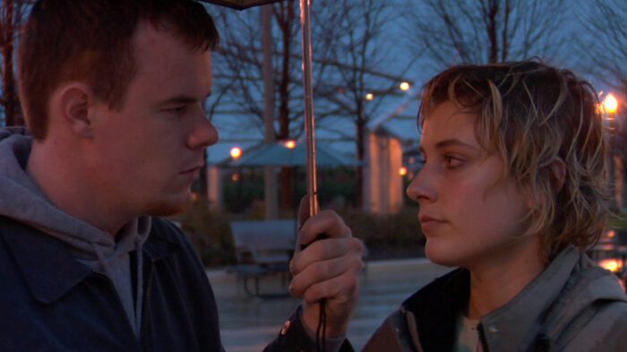 Close up of James (Joe Swanberg) and Mattie (Greta Gerwig) looking at each other under an umbrella at night.