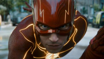 The Flash (Ezra Miller) gets into his running stance while wearing his red costume with yellow lightning streaks.
