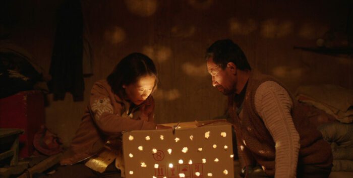 A Chinese man and woman sit over a homemade incubator which lillumiates their faces.