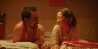 A Chinese man and woman smile at each other in bed.