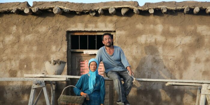 A Chinese man and woman pose in front of a hand-built mudhouse.
