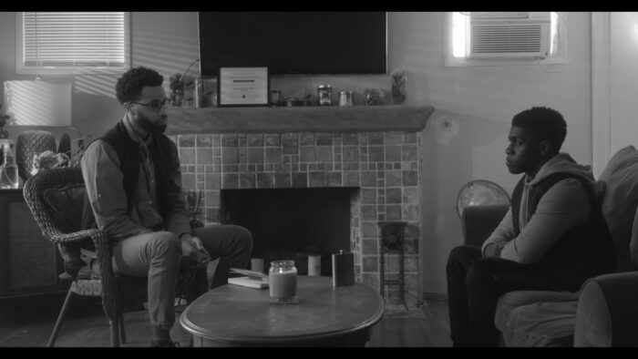 Two young black men engage in conversation in a living room.