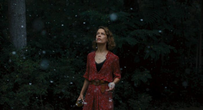 a A young woman in a red dress stares at flakes of ash falling from the sky in Afire