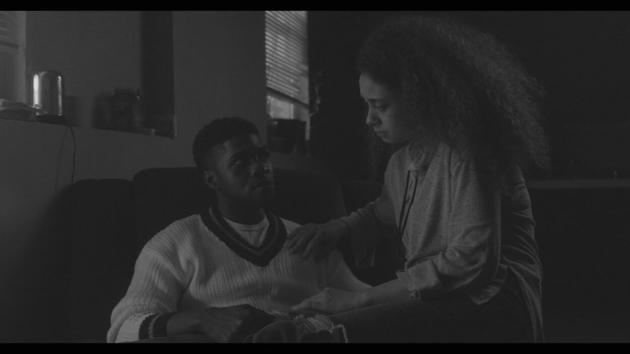 A young black man and woman converse on a sofa.