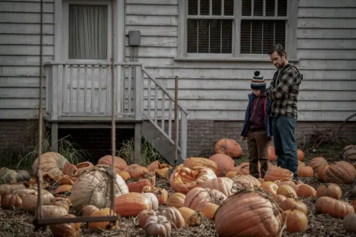 Image from COBWEB. Shows a boy and his father standing in a garden full of smashed and blighted pumpkins. 