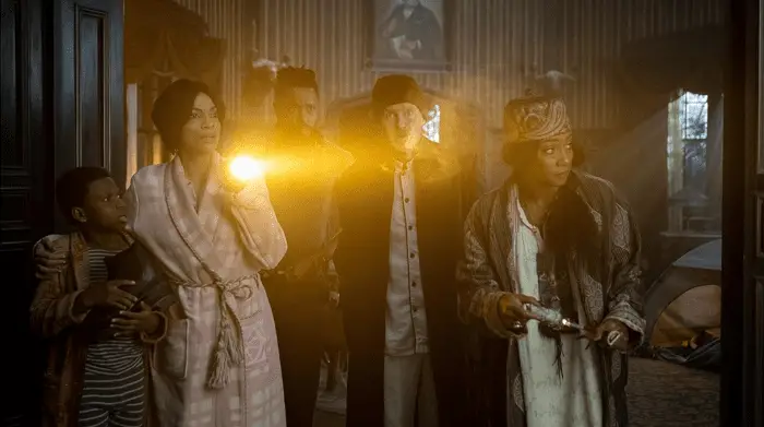 Haunted Mansion: l-r Travis (Chase Dillon), Gabbie (Rosario Dawson), Ben Matthias (LaKeith Stanfield), Father Kent (Owen Wilson) and Harriet (Tiffany Haddish) looking out of the living room at midnight. 