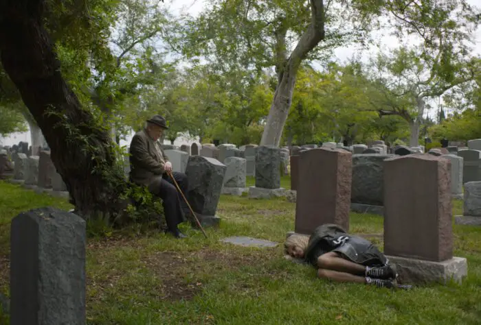 An old man sits near a teen sleeping in a cemetery in Tiger Within