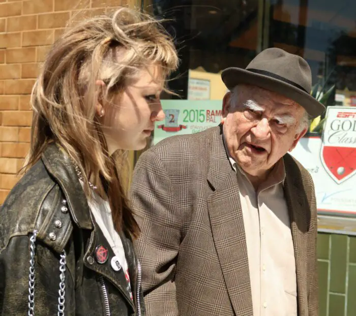 A teen and an older man talk while walking down a street.