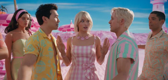 Two competitive men face off with a woman in-between them at the beach in Barbie.