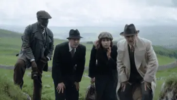 Four people stare at the ground on an English countryside in the 1930s.