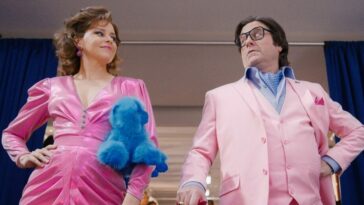 Elizabeth Banks and Zach Galifianakis wear bright pink outfits to attract attention at a toy expo where their characters intend to sell Beanie Babies.