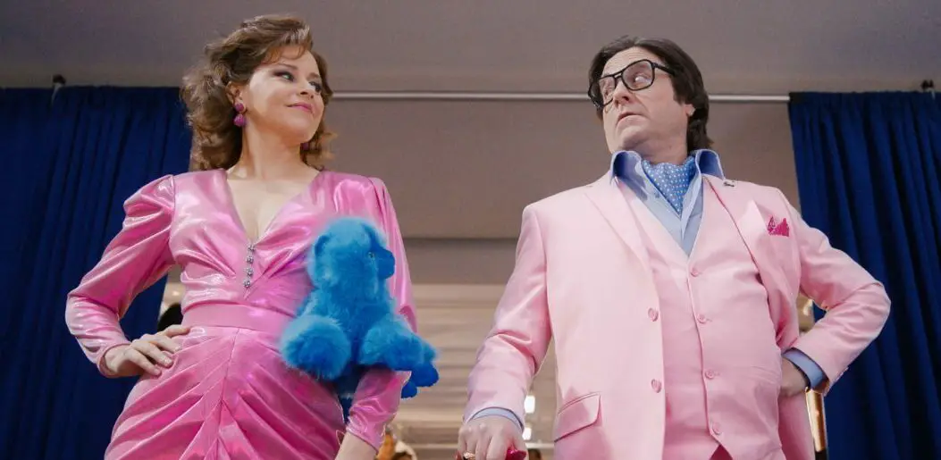 Elizabeth Banks and Zach Galifianakis wear bright pink outfits to attract attention at a toy expo where their characters intend to sell Beanie Babies.