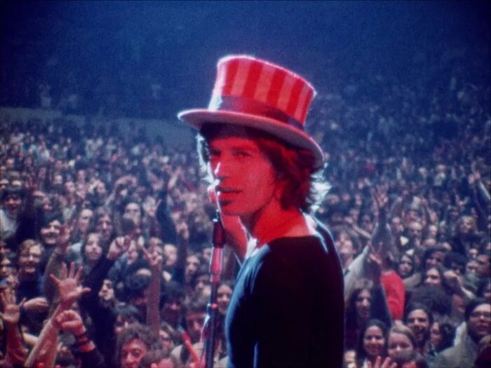 Mick Jagger, wearing a stars-and-stripes top hat, looks at the camera from the stage.