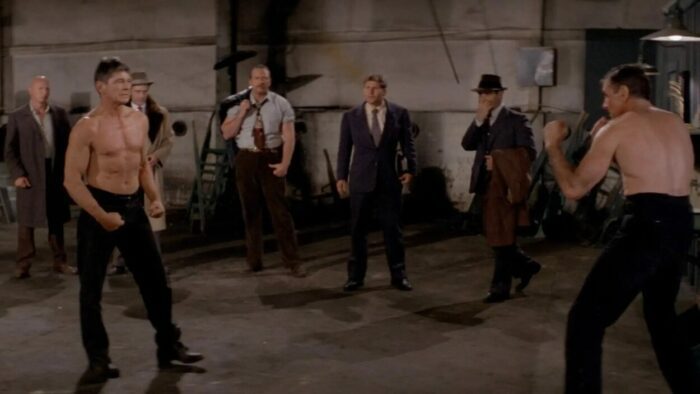 A shirtless Chaney prepares to fight another man in a warehouse.