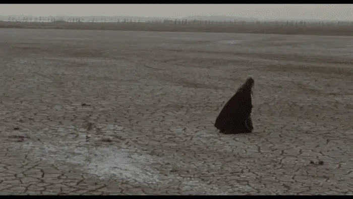Medea walks alone across an empty field.