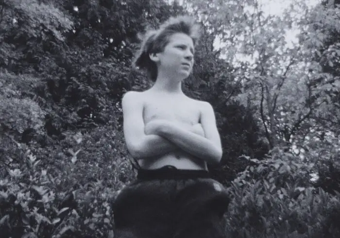 A shirtless boy poses in the woods.