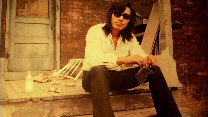 1960s singer Rodriguez poses on a concrete stoop.