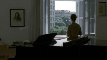 A woman standing behind the piano and looking out of the window
