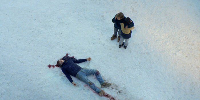 A man lies dead on the snow as his wife and son look on him in fear.
