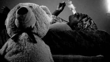 Liyah lays on her bed, smoking with a large teddy bear next to her