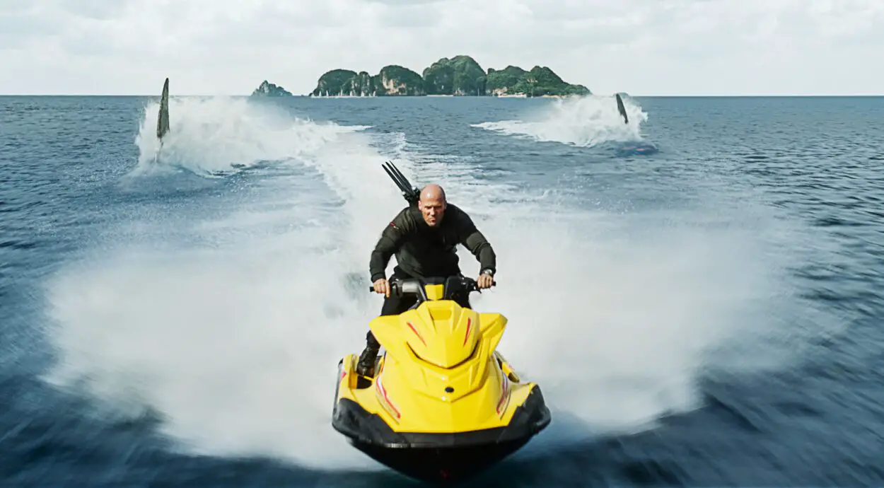 A man on a jet ski attempts to outrun three large sharks in The Meg 2: The Trench