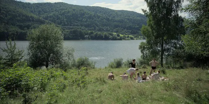 A family lounges in a field by water in The Zone of Interest from TIFF 2023