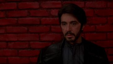 A man stands in front of a red painted brick wall in Carlito's Way