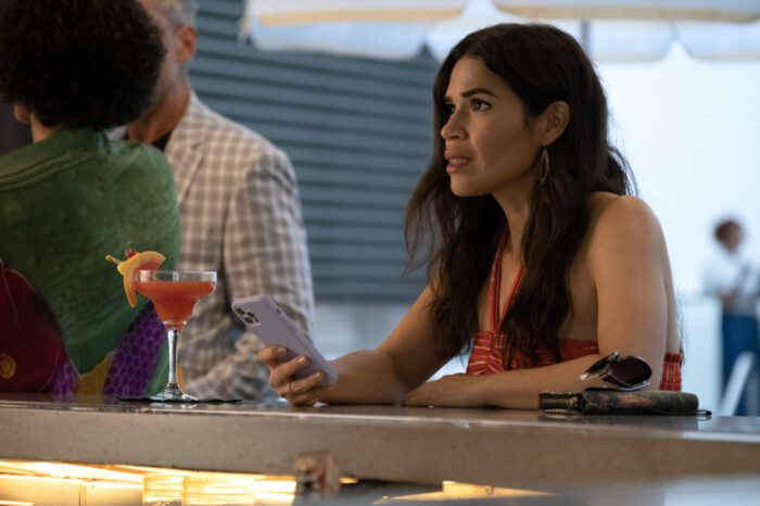 Jennifer (America Ferrera) sips a margarita at a bar with her phone in her hand as she looks up receiving some worrying and surprising news.