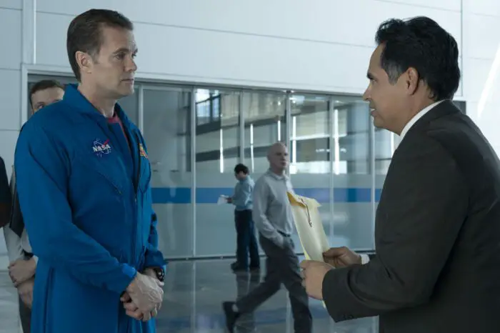 A man in a suit confronts an astronaut in a lobby.