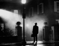 A man with a fedora and handbag stands in silhouette with a street light in The Exorcist.