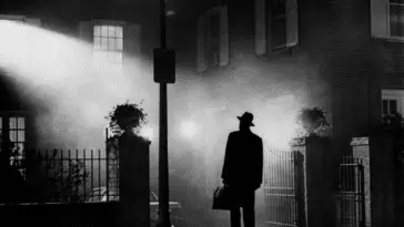 A man with a fedora and handbag stands in silhouette with a street light in The Exorcist.