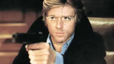 A man in glasses holds up a pistol in Three Days of the Condor