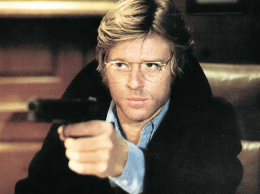 A man in glasses holds up a pistol in Three Days of the Condor