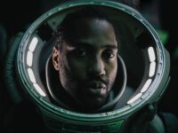 Joshua (John David Washington), wearing a spacesuit), looks intently on with lights illuminating him.