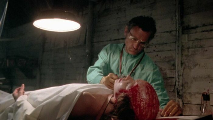 The mad doctor stands over a victim laying on a table with her head scalped.