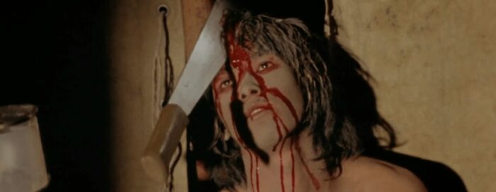 A cannibal leaning against a wall with a machete in his head.