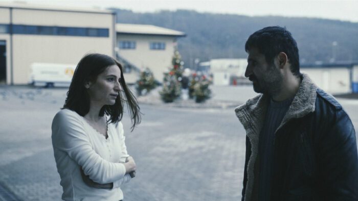 A man and a woman converse on a street.