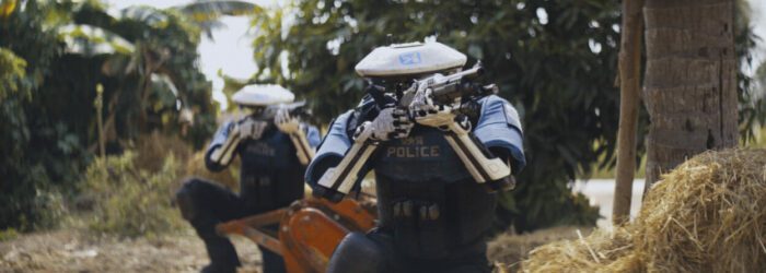 The world of The Creator features android robots, some of which are officers, seen here in a forest with guns as they hunt someone.