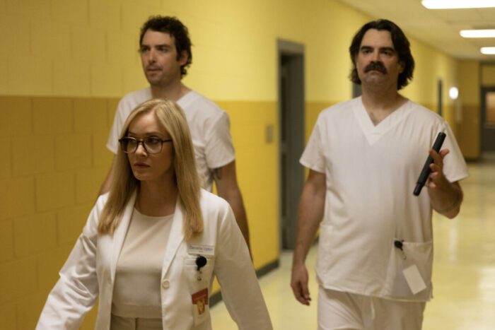Daniella Upton (Barbara Crampton) walks down a hospital corridor with two orderlies behind her in Suitable Flesh (2023). 
