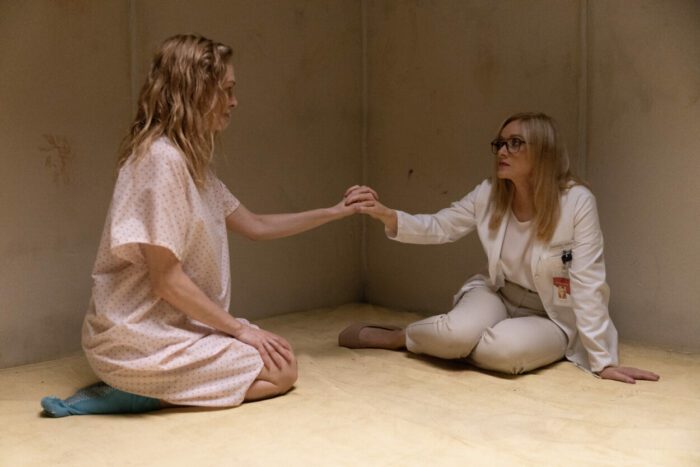 Wearing a lab coat, Dr. Daniella Upton (Barbara Crampton) reaches out to Dr. Elizabeth Derby (Heather Graham), wearing a hospital gown, in a padded cell.