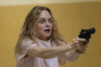 Elizabeth Derby (Heather Graham), wearing a hospital gun and a crazed look, wields a gun.
