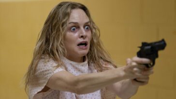 Elizabeth Derby (Heather Graham), wearing a hospital gun and a crazed look, wields a gun.
