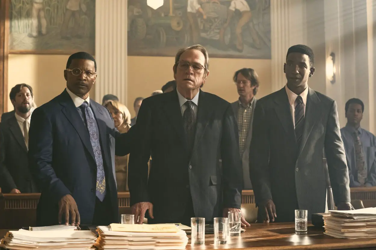 A white man stands between his two Black lawyers in court in The Burial
