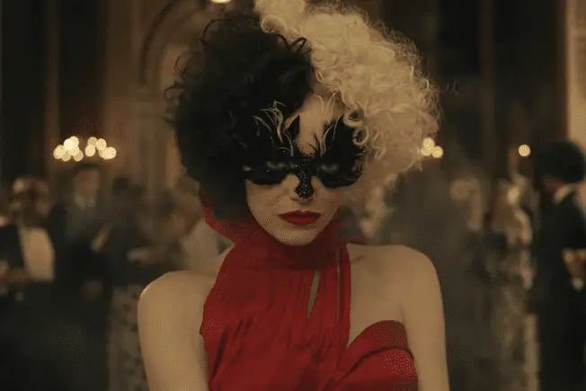 Emma Stone as Cruella with black face paint, wearing a red dress and curly hair that's half black and half white.