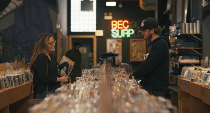 A man and woman chat across the racks of a record store.