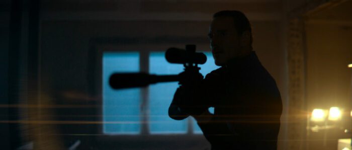 A man in shadow holds a sniper rifle at the ready in The Killer.
