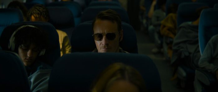 A man wearing sunglasses sits on a plane.
