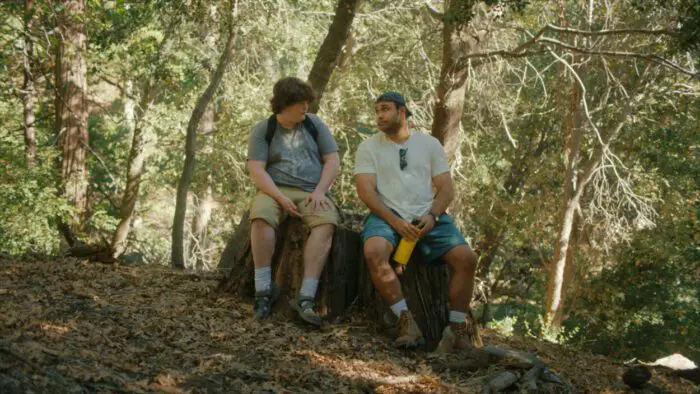 Jamie and Dan sit next to each other on a log in the middle of the woods